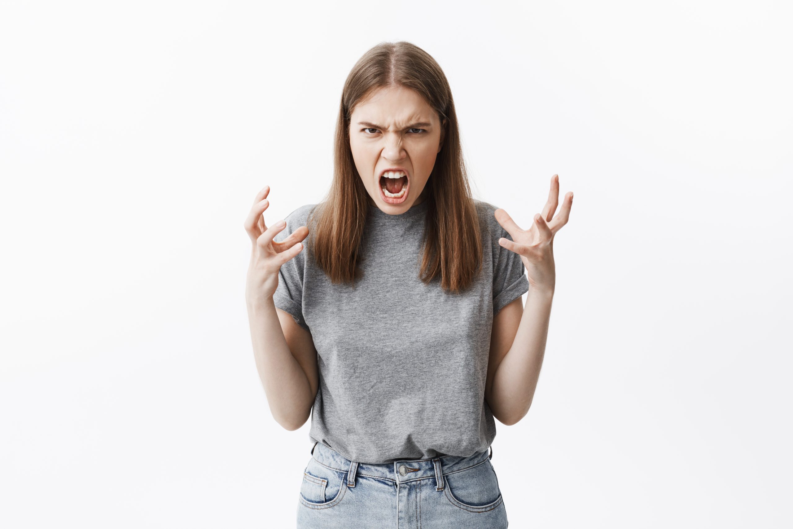Close up portrait of mad beautiful caucasian student girl with brown hair in casual clothes looking in camera with angry face expressions, gesticulated with hands, being pissed off she broke her bew smartphone.